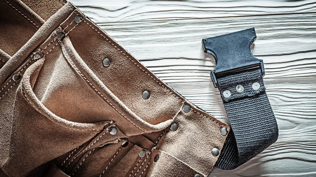 Leather tool pouch with a belt hanger laid on a grey wood bench