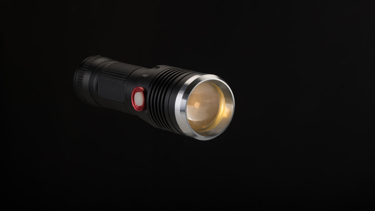 Compact black flashlight switched on against a black background