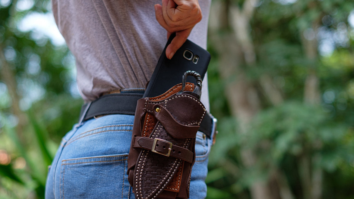 Person outdoors sliding a phone into a leather belt holster