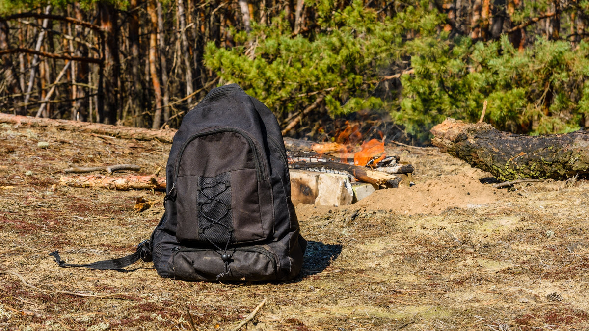 Black backpack on the ground beside a campfire in the woods