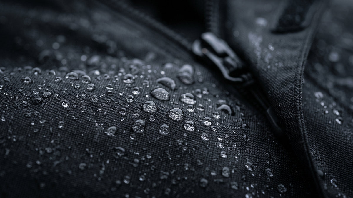 Rain beading on black coated nylon beside a zipper with a storm flap